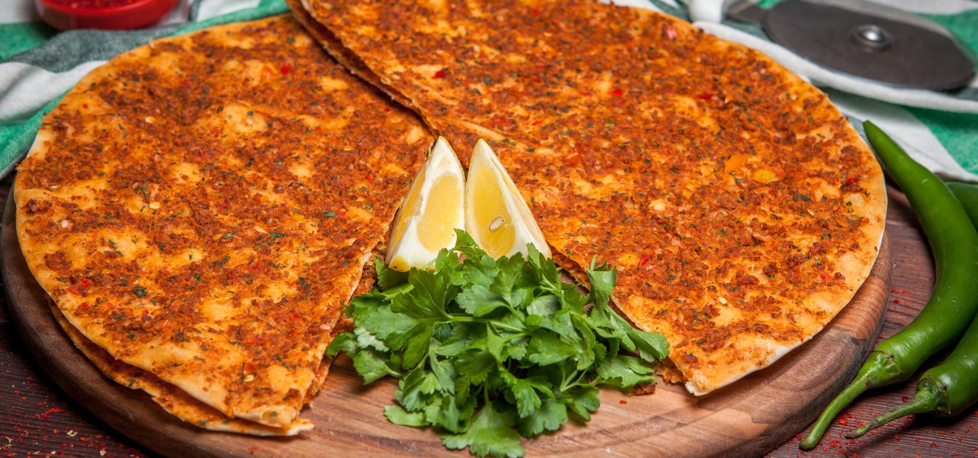 Side view lahmacun with lemon and parsley and green pepper in board cookware on wooden background